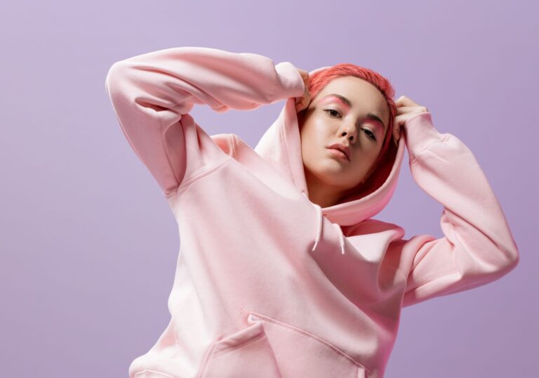 Fashionable woman in pink hoodie and skirt against a violet backdrop.